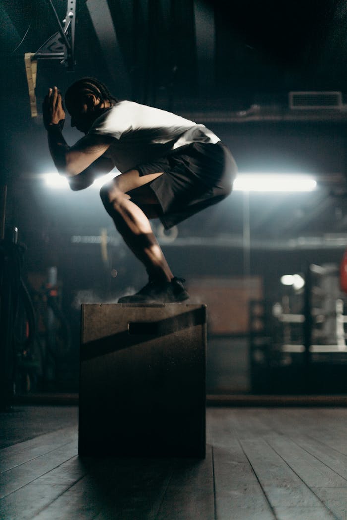 services-03 Silhouette of a man performing a box jump in a dimly lit gym, highlighting strength and agility.