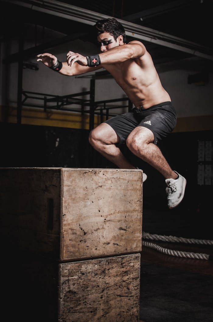 services-02 Shirtless man showcasing strength and fitness with a box jump in an indoor gym setting.